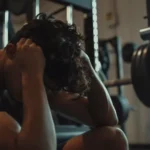 Hombre mostrando signos de catabolismo muscular y fatiga después de un entrenamiento intenso en el gimnasio