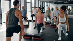 Clase colectiva de gimnasio con varias personas entrenando con mancuernas y step, representando cómo elegir clases colectivas según objetivo